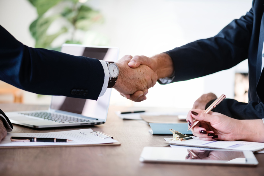 Two people shaking hands over a table with papers.